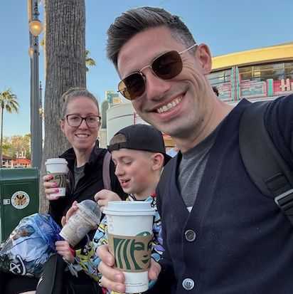 Aaron Aiken A picture of Aaron Aiken, smiling directly at the camera, on a bench with his family enjoying beverages from Starbucks.